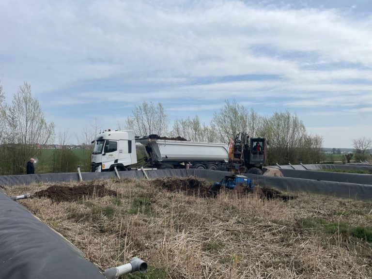 Curage bassin assainissement : pelle des ETS Delestrez chargeant les sédiments dans une benne céréalière au bord du bassin